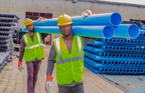 Ouvriers IBP sur le site de l’usine à Cotonou transportant des tuyaux PVC pour chargement avec équipements de protection individuelle