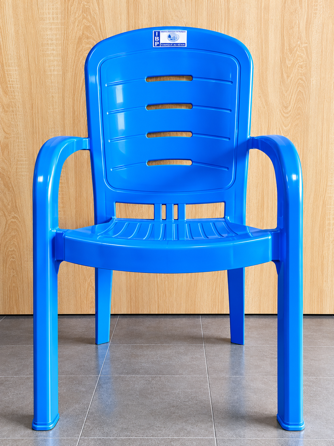 Chaise en plastique bleu grand format IBP avec accoudoirs et dossier ajouré à quatre ouvertures horizontales, fabriquée au Bénin.