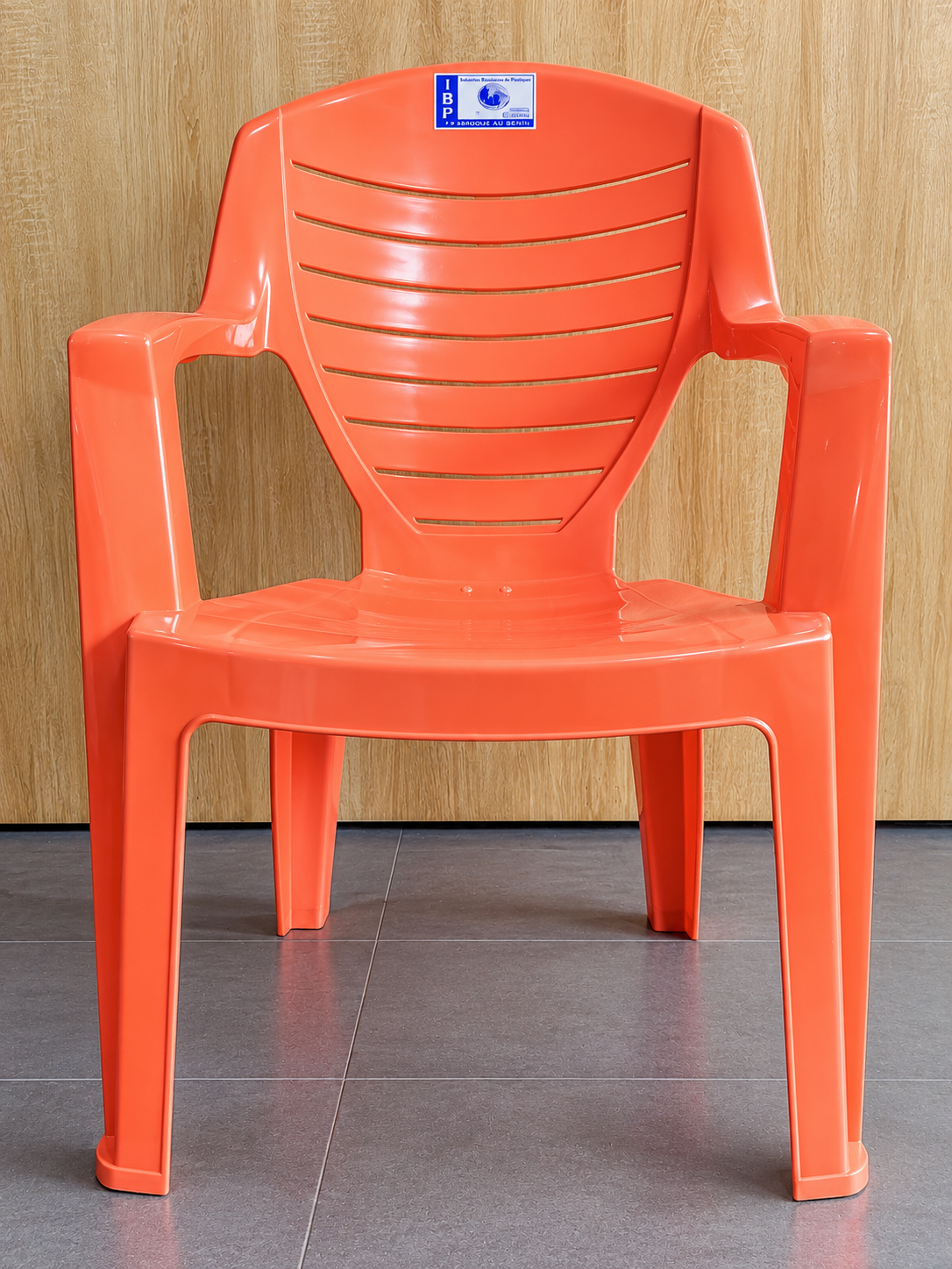 Chaise en plastique orange petit format IBP avec accoudoirs, dossier à rainures horizontales et logo IBP, fabriquée au Bénin.